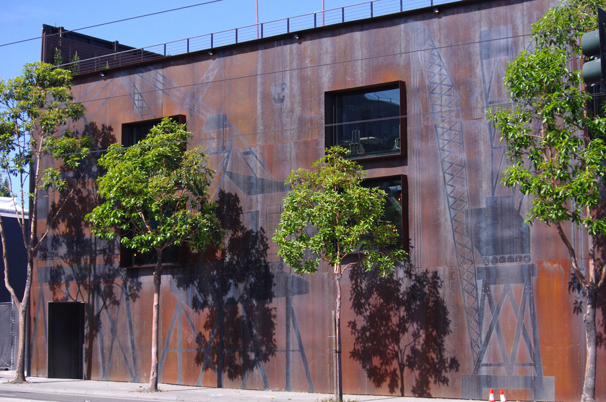 The weathered steel facade of The Pearl, the multi-level Dogpatch venue in San Francisco hosting the Summit, with street trees in front
